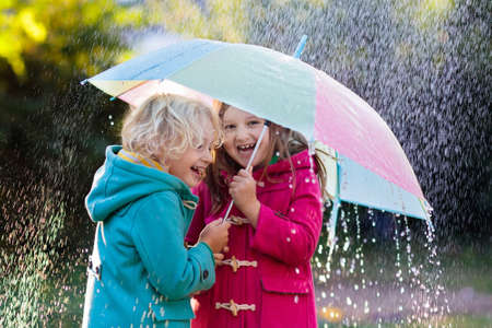 Kids with colorful umbrella playing in autumn shower rain. Coat in rainy weather. Fall outdoor fun for children. Kid catching rain drops.の写真素材