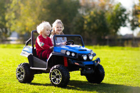 Kids driving electric toy car in summer park. Outdoor toys. Children in battery power vehicle....