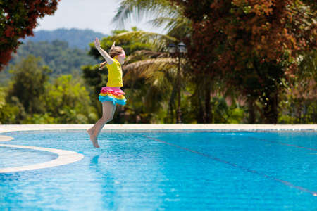 Child playing in swimming pool. Summer vacation with kids. Little girl jumping into water during exotic holiday in tropical island resort. Children swim. Active outdoor sport for preschooler.の写真素材