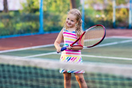 Child playing tennis on outdoor court. Little girl with tennis racket and ball in sport club. Active exercise for kids. Summer activities for children. Training for young kid. Child learning to play.の写真素材