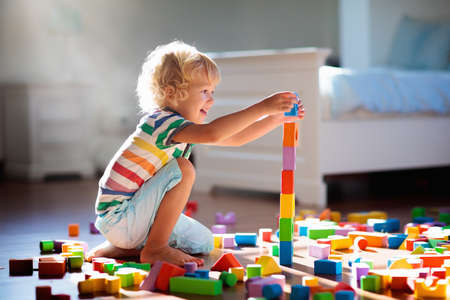 Child playing with colorful toy blocks. Kids play. Little boy building tower of block toys sitting on dark floor in sunny white bedroom. Educational game for baby and toddler. Children build toy houseの写真素材