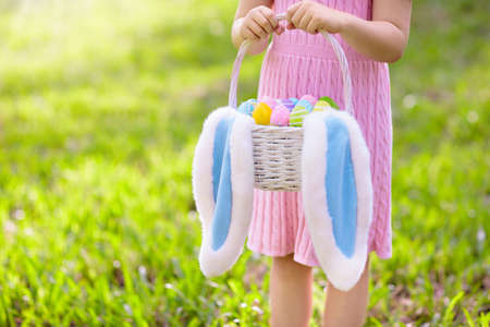 Kids with eggs basket and bunny ears on Easter egg hunt in sunny spring garden. Little girl...