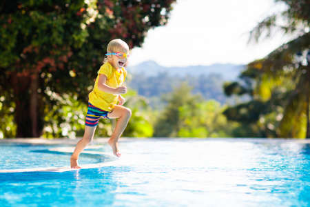 Child playing in swimming pool. Summer vacation with kids. Little boy jumping into water during exotic holiday in tropical island resort. Children swim. Active outdoor sport for preschooler.の写真素材