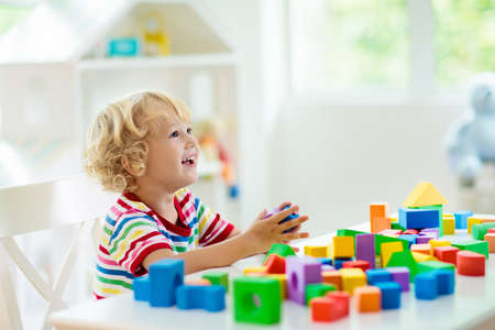 Kid playing with colorful toy blocks. Little boy building tower of block toys. Educational and creative toys and games for young children. Baby in white bedroom with rainbow bricks. Child at home.の写真素材