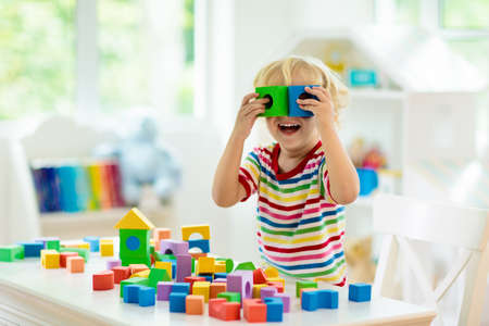 Kid playing with colorful toy blocks. Little boy building tower of block toys. Educational and creative toys and games for young children. Baby in white bedroom with rainbow bricks. Child at home.の写真素材