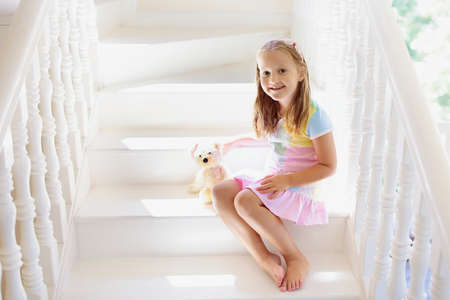 Kid walking stairs in white house. Little girl playing in sunny staircase. Family moving into new home. Child climbing steps of modern stairway. Foyer or living room interior. Home safety for toddler.の写真素材