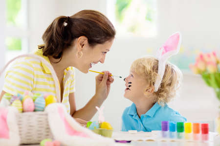 Mother and kids color Easter eggs. Face painting for little child. Little boy with bunny ears and mom dye eggs. Easter egg hunt. Family celebration and home decoration for spring holiday.の写真素材