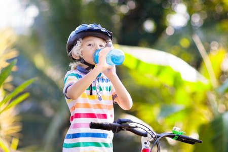 Kids on bike in park. Children going to school wearing safe bicycle helmets. Little boy biking on sunny summer day. Active healthy outdoor sport for young child. Fun activity for kid.の写真素材