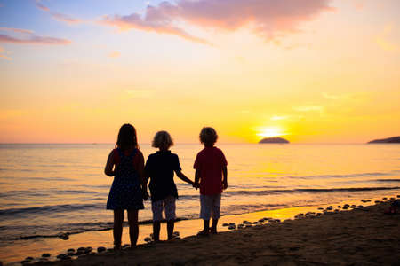 Child playing on ocean beach. Kid jumping in the waves at sunset. Sea vacation for family with kids. Summer island during summer holidayの写真素材