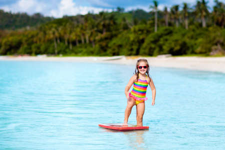 Child surfing on tropical beach. Family summer vacation in Asia. Kids swim in ocean water. Kid on surf body board. Little girl swimming in exotic sea. Travel with children. Water and beach sport.の写真素材
