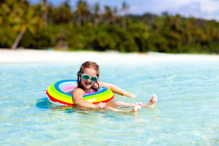 Child with inflatable ring on beautiful beach. Little girl swimming in exotic sea. Ocean vacation with kid. Children play on summer beach. Water fun. Kids swim. Family holiday on tropical island.の写真素材