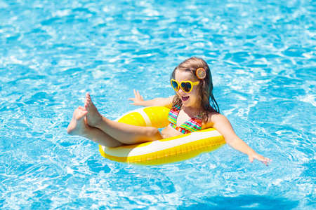 Child in swimming pool on inflatable yellow lemon ring. Little girl learning to swim with orange...