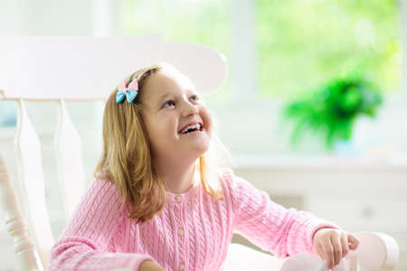 Child playing with baby cat. Kid holding white kitten. Little girl with cute pet animal sitting on couch in sunny living room at home. Kids play with pets. Children and domestic animals.の写真素材