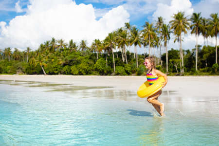 Child playing on tropical beach. Little girl with inflatable float ring at sea shore. Family summer vacation. Kids play with water and sand toys. Swimming fun. Travel with young children. Asia holidayの写真素材