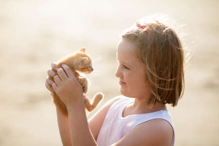 Child holding baby cat. Kids and pets. Little girl hugging cute little kitten in summer garden....