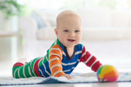 Adorable baby boy learning to crawl and playing with colorful rainbow ball toy in white sunny...