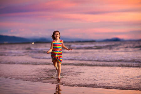 Child playing on ocean beach. Kid jumping in the waves at sunset. Sea vacation for family with kids. Little girl running on tropical beach of exotic island during summer holiday.の写真素材