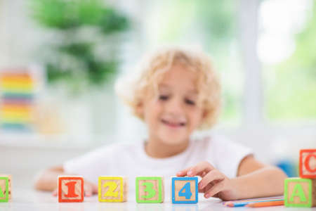 Child learning letters and numbers. Kid with colorful wooden abc blocks. Little boy spelling words with educational block toys. Kids doing school homework at white desk. Bedroom for preschool childrenの写真素材