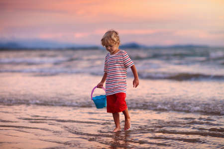 Child playing on ocean beach. Kid jumping in the waves at sunset. Sea vacation for family with kids. Little boy running on tropical beach of exotic island during summer holiday.の写真素材