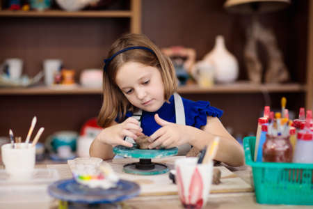 Child working on pottery wheel. Kids arts and crafts class in workshop. Little girl creating cup and bowl of clay. Creative activity for young children in school. Cute kid forming toy with ceramic.の写真素材