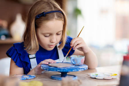 Child working on pottery wheel. Kids arts and crafts class in workshop. Little girl creating cup and bowl of clay. Creative activity for young children in school. Cute kid forming toy with ceramic.の写真素材