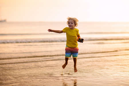 Child playing on ocean beach. Kid jumping in the waves at sunset. Sea vacation for family. Little boy running on exotic island during summer holiday.の写真素材