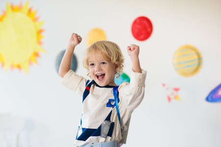 Kids play astronaut. Little boy in space costume jumping on bed with rocket. Solar system and planet room decoration. Creative child, future profession.の写真素材