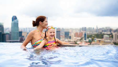 Children swimming in roof top outdoor pool on family vacation in Singapore. City skyline from infinity pool in luxury hotel. Kids swim and enjoy skyscraper view in Asia. Travel with young child.の写真素材