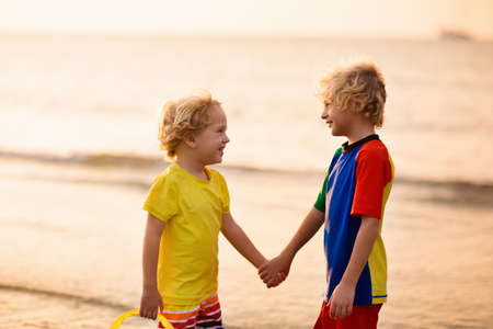 Child playing on ocean beach. Kid jumping in the waves at sunset. Sea vacation for family. Little boy running on exotic island during summer holiday. Brothers love. Siblings hug, hold hands.の写真素材
