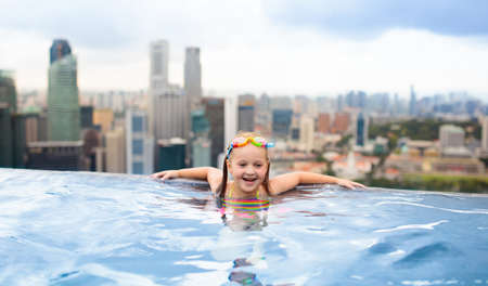 Children swimming in roof top outdoor pool on family vacation in Singapore. City skyline from infinity pool in luxury hotel. Kids swim and enjoy skyscraper view in Asia. Travel with young child.の写真素材