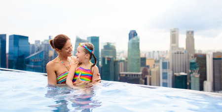 Children swimming in roof top outdoor pool on family vacation in Singapore. City skyline from infinity pool in luxury hotel. Kids swim and enjoy skyscraper view in Asia. Travel with young child.の写真素材