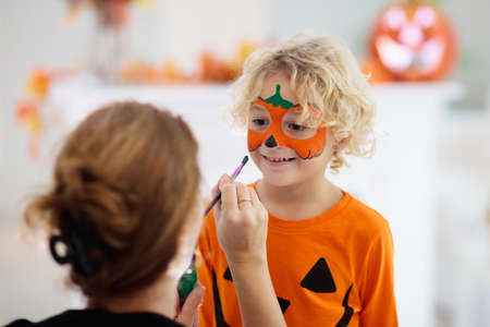 Child and mother in Halloween costume. Kids trick or treat. Face painting for party event. Little boy dressed as evil vampire with pumpkin lantern. Family celebration. Mom and son with candy.の写真素材