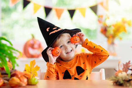 Child in Halloween costume. Kids trick or treat. Little boy with pumpkin lantern. Baby in witch hat. Autumn season holiday decoration. Home festive interior with fall leaves and squash.の写真素材