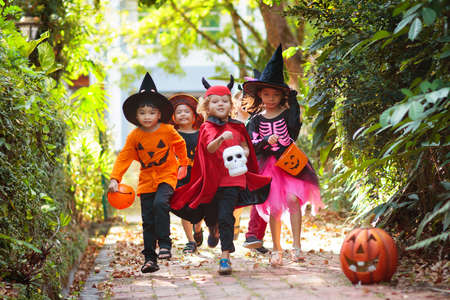 Child in Halloween costume. Mixed race Asian and Caucasian kids trick or treat on suburban street. Little boy and girl with pumpkin lantern and candy bucket. Baby in witch hat. Autumn holiday fun.の写真素材