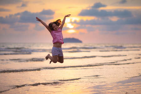 Child playing on ocean beach. Kid jumping in the waves at sunset. Sea vacation for family with kids. Little girl running on  exotic island during summer holiday. の写真素材