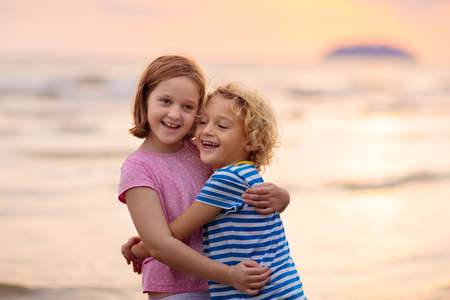 Child playing on ocean beach. Kid jumping in the waves at sunset. Sea vacation for family. Little...