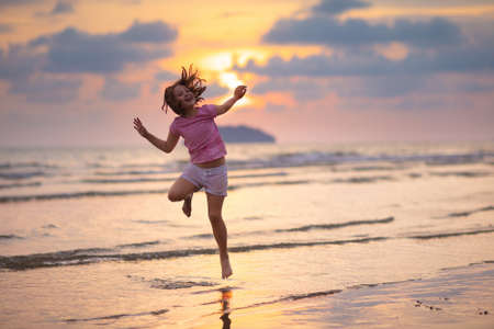Child playing on ocean beach. Kid jumping in the waves at sunset. Sea vacation for family with kids. Little girl running on  exotic island during summer holiday.の写真素材