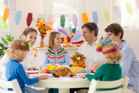 Family with kids eating Thanksgiving dinner. Roasted turkey and pumpkin pie on dining table with autumn decoration. Parents and children festive meal. Father and mother cutting meat. Paper crafts hat.の写真素材