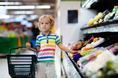 Child in supermarket buying fruit and juice. Kid grocery shopping. Little boy with cart choosing fresh vegetables in local store.の写真素材