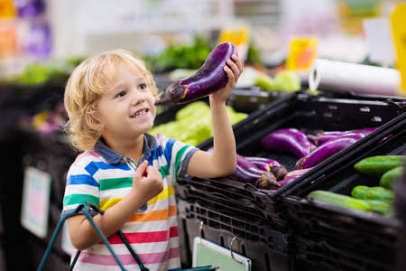 Child in supermarket buying fruit and juice. Kid grocery shopping. Little boy with cart choosing fresh vegetables in local store.の写真素材