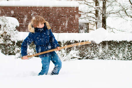 Child shoveling snow. Little boy with spade clearing driveway after winter snowstorm. Kids clear path to house door after Christmas blizzard. Snowfall fun. Children play in cold frosty garden.の写真素材
