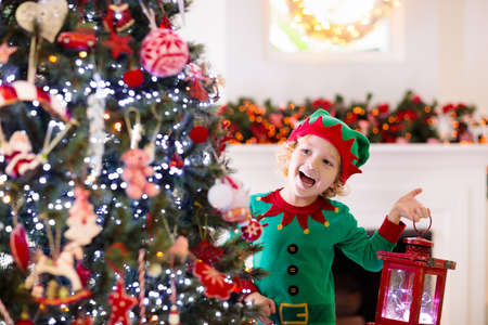 Child decorating Christmas tree at home. Little boy in elf costume and hat with Xmas ornament....