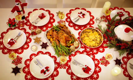 Christmas dinner at fireplace and decorated Xmas tree. Dish with roasted turkey, salad and baked potato served for festive family meal. Wine bottle with Santa hat. Open fire in stone oven.の写真素材