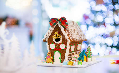 Gingerbread house for Christmas. Baking with kids for winter holidays. Decorated tree and candle lights in living room with fireplace. Pastry and sweets.の写真素材