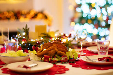 Christmas dinner at fireplace and decorated Xmas tree. Dish with roasted turkey, salad and baked potato served for festive family meal. Wine bottle with Santa hat. Open fire in stone oven.の写真素材