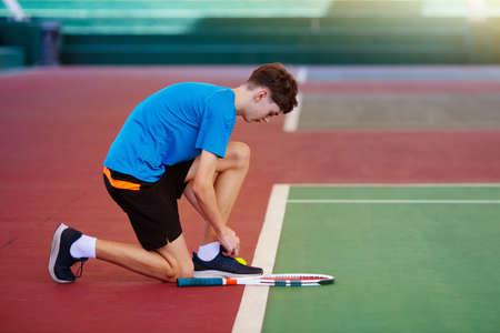Young man playing tennis on open court. Teenager with racquet at competition match. Healthy outdoor sport for high school or college kids. Student exercising.の写真素材
