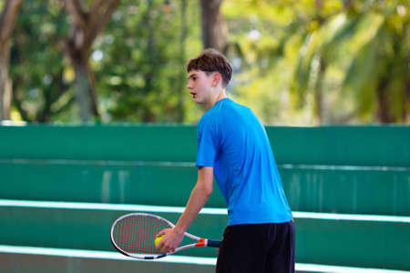 Young man playing tennis on open court. Teenager with racquet at competition match. Healthy outdoor sport for high school or college kids. Student exercising.の写真素材