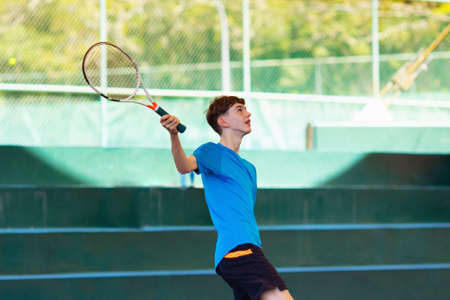Young man playing tennis on open court. Teenager with racquet at competition match. Healthy outdoor sport for high school or college kids. Student exercising.の写真素材