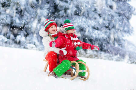 Little girl and boy enjoying sleigh ride. Child sledding. Toddler kid riding a sledge. Children play outdoors in snow. Kids sled in snowy park in winter. Outdoor fun for family Christmas vacation.の写真素材