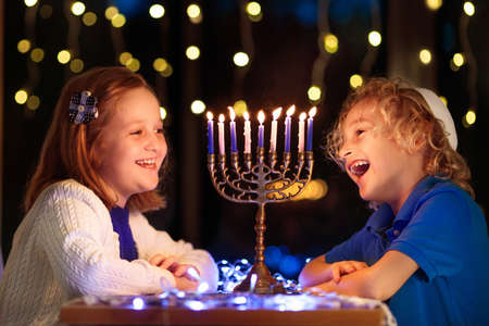 Kids celebrating Hanukkah. Jewish festival of lights. Children lighting candles on traditional menorah. Boy in kippah with dreidel and Sufganiyah doughnut. Israel holiday.の写真素材